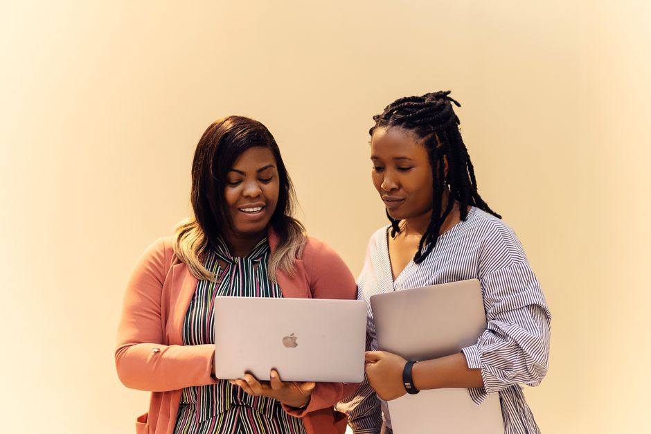 Two professional women collaborating on laptops while registering their business